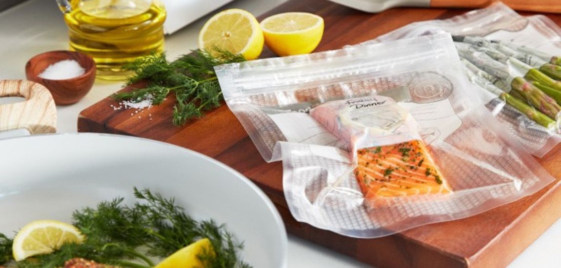 Łosoś oraz szparagi zapakowane próżniowo w worku FoodSaver, leżące na drewnianej desce do krojenia